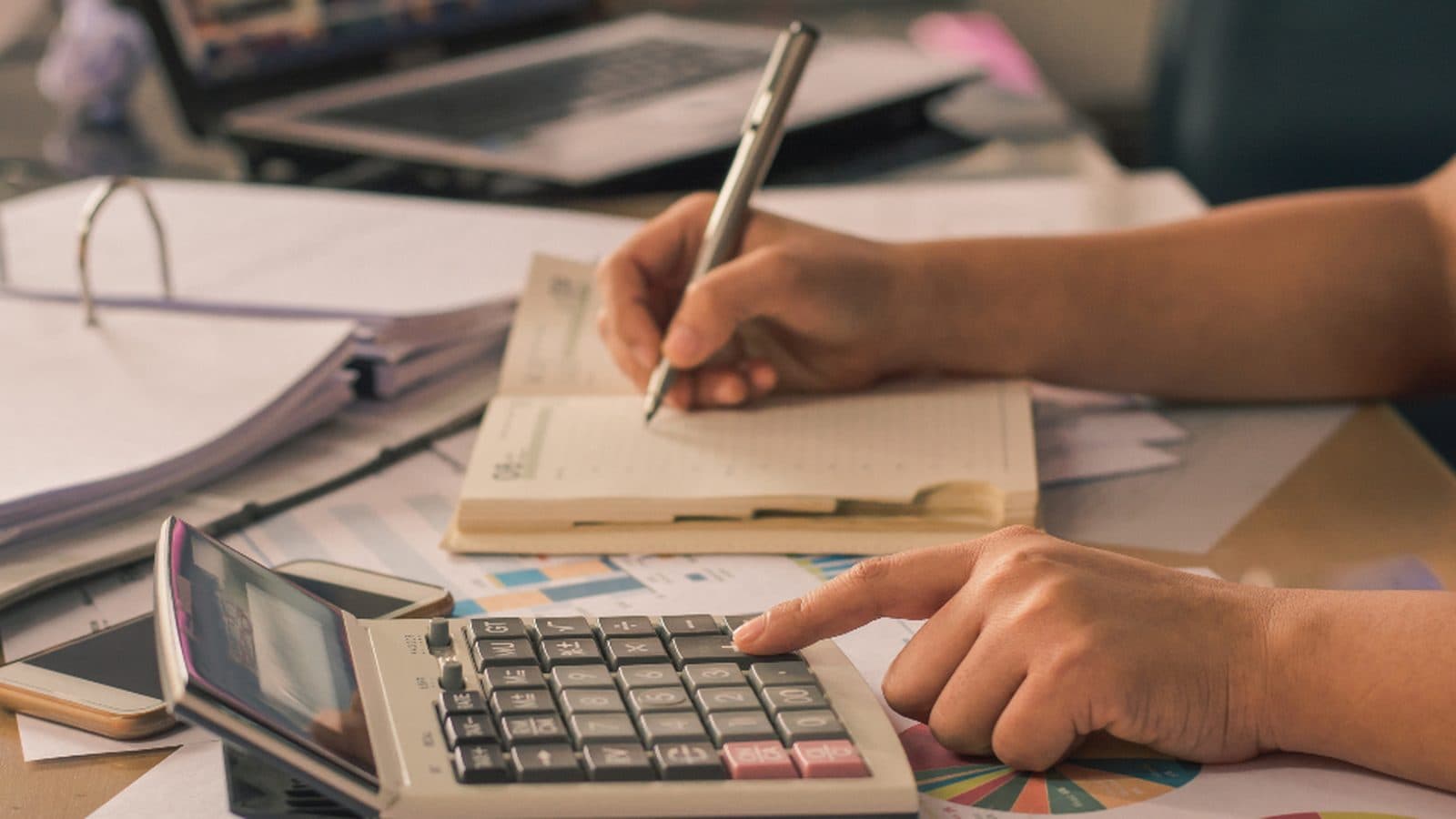 Mãos fazendo contas com calculadora sobre papéis e recibos