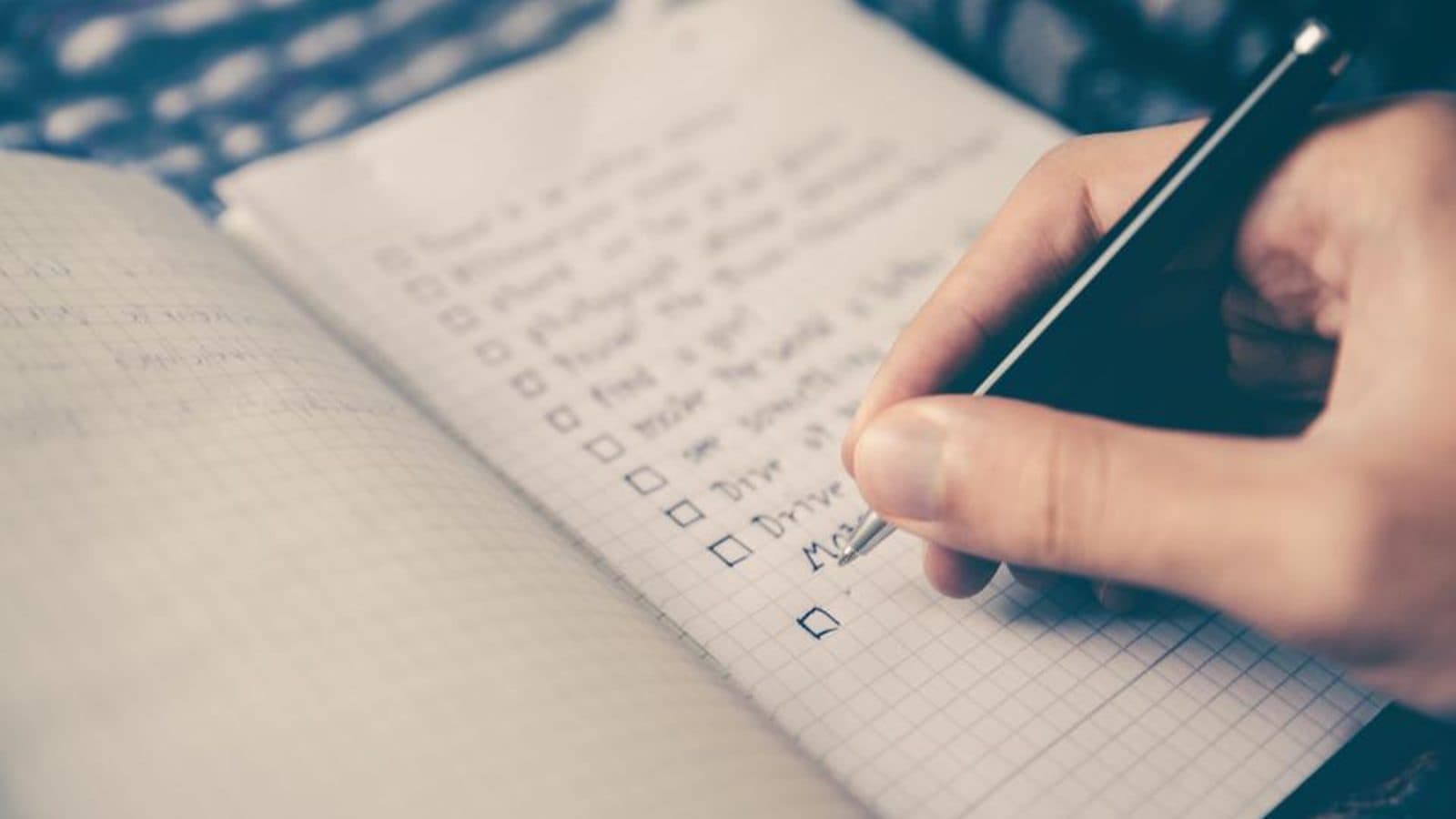 Mão escrevendo em uma lista de itens num caderno