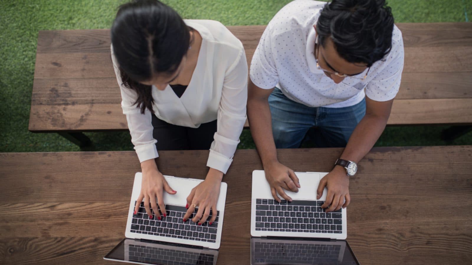 Duas pessoas lado a lado trabalhando em notebooks, vistas de cima