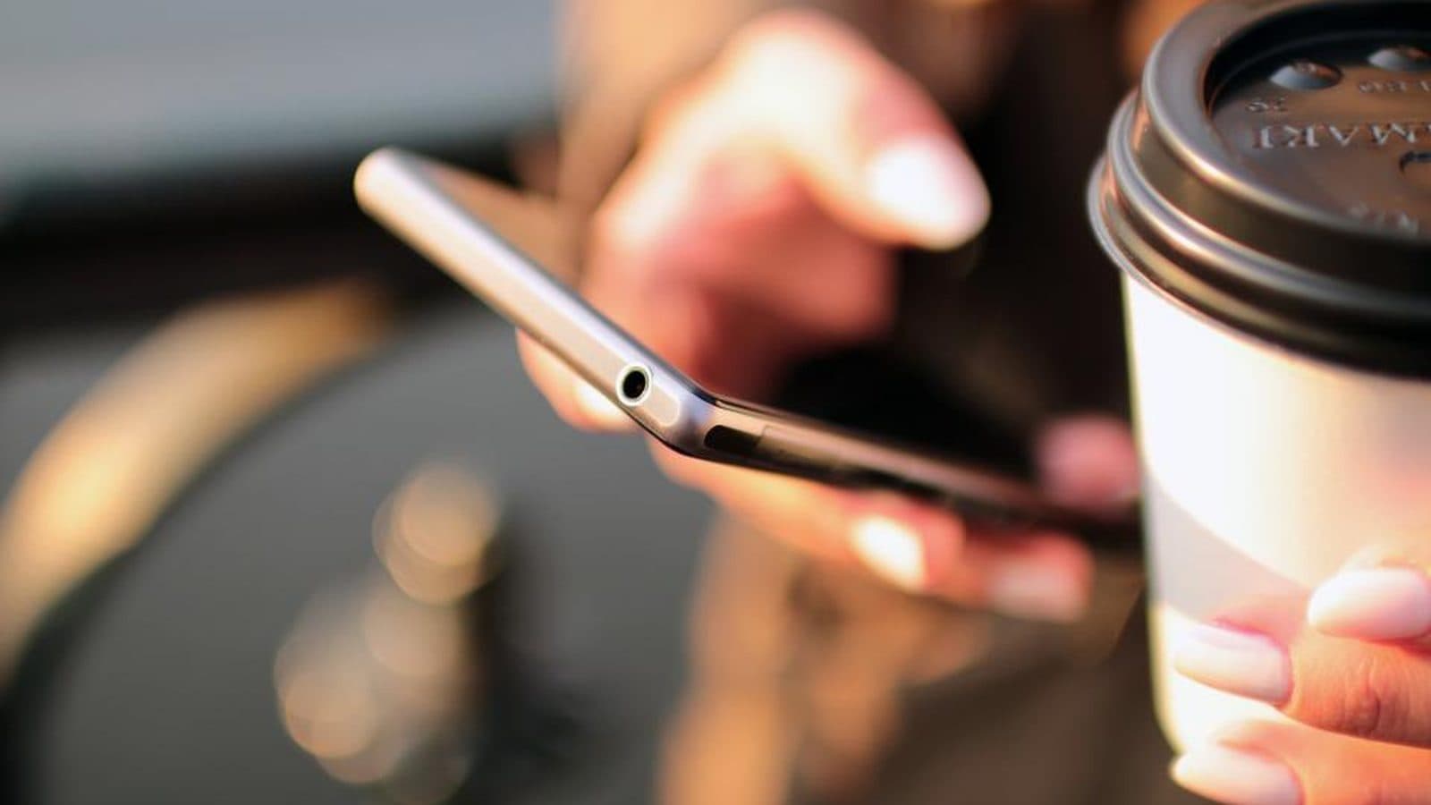 Mão segurando um celular, com uma xícara de café ao lado