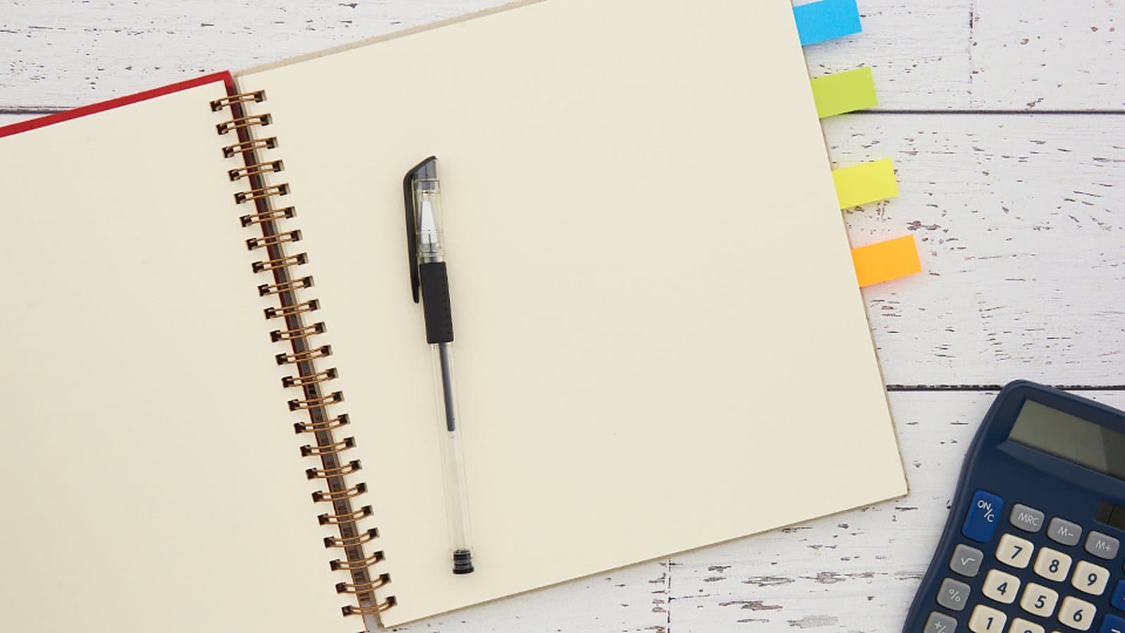 Caderno espiral aberto em página em branco, com caneta, marcadores coloridos e calculadora