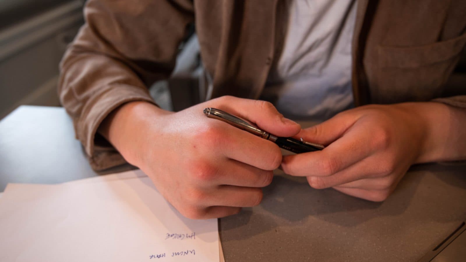 Pessoa escrevendo em um caderno sobre uma mesa, com papéis ao lado